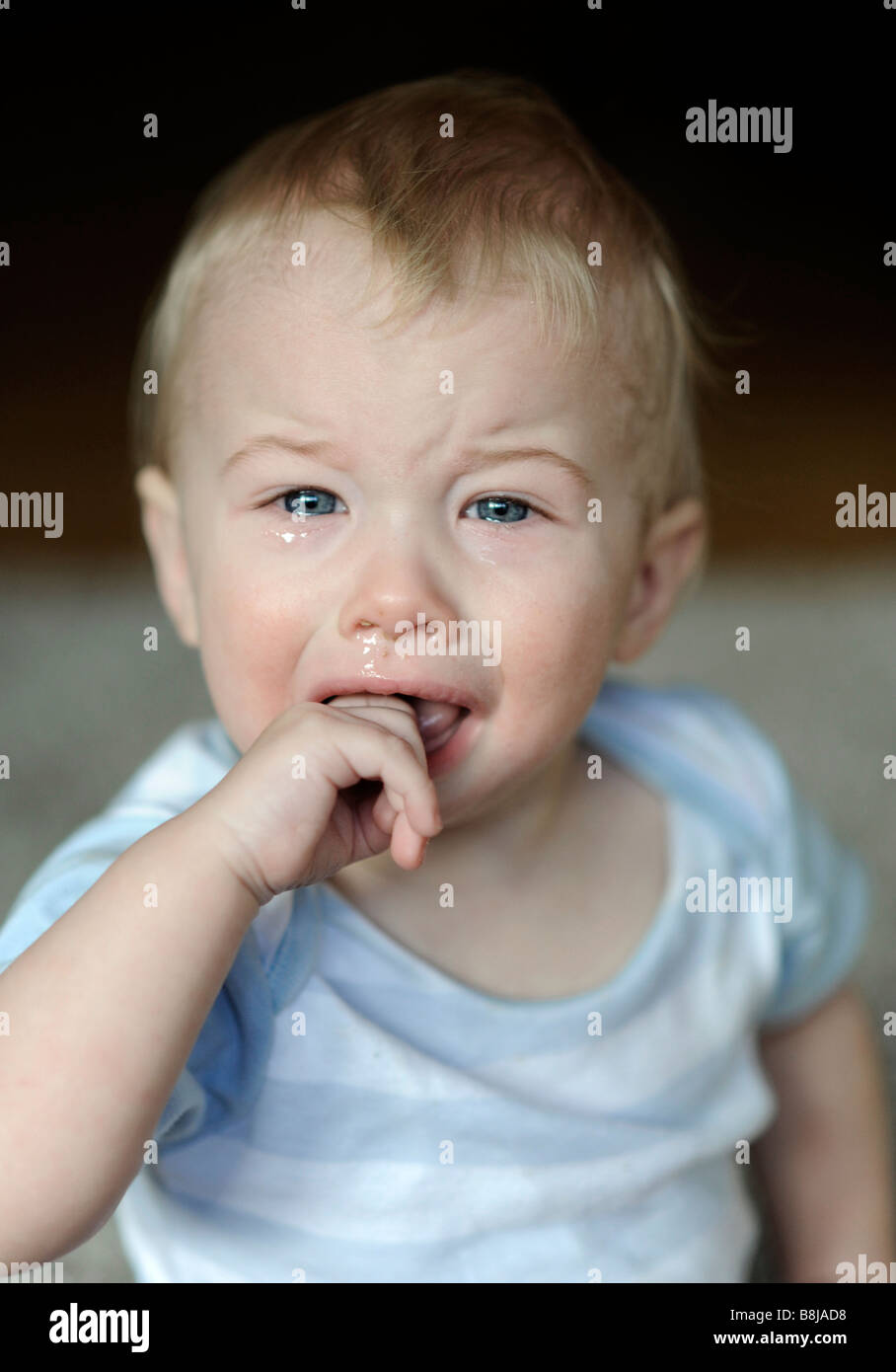 A baby boy with blue eyes puts his fingers into his mouth while he
