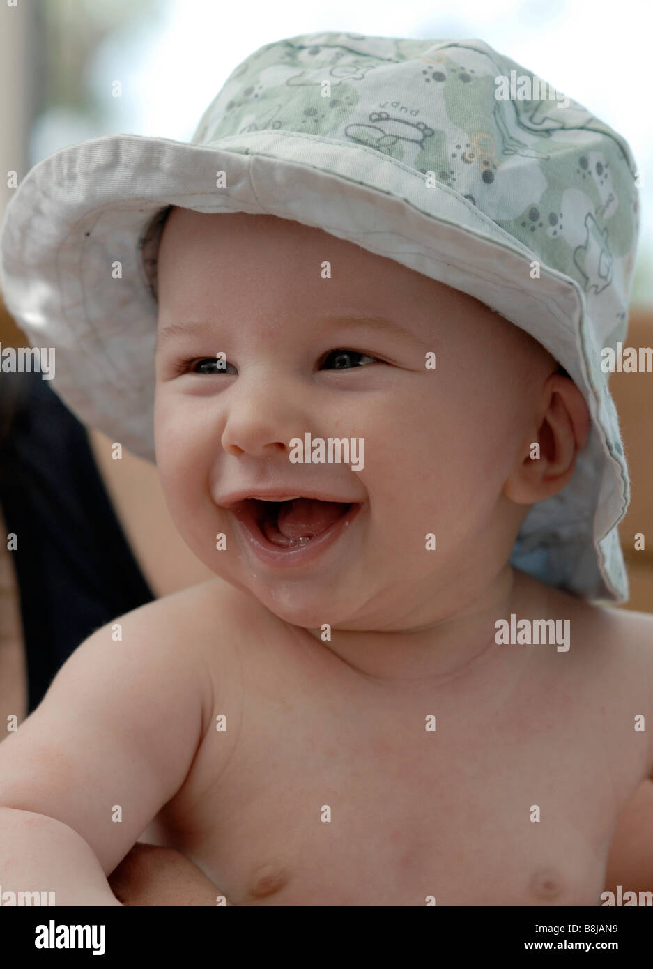 A baby boy with blue eyes smiles and chuckles while wearing a sun hat