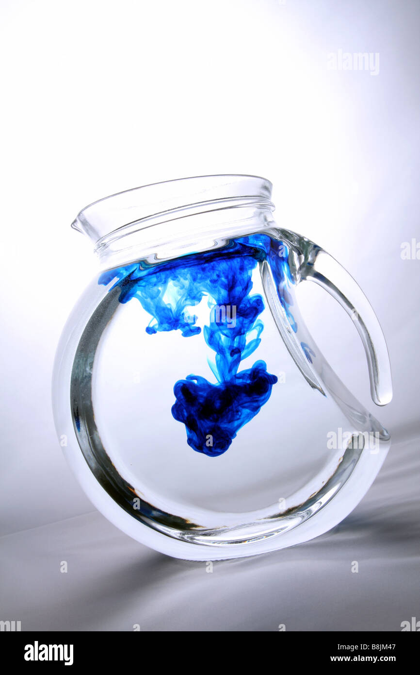 Food coloring dispersing in a jug of water. Stock Photo
