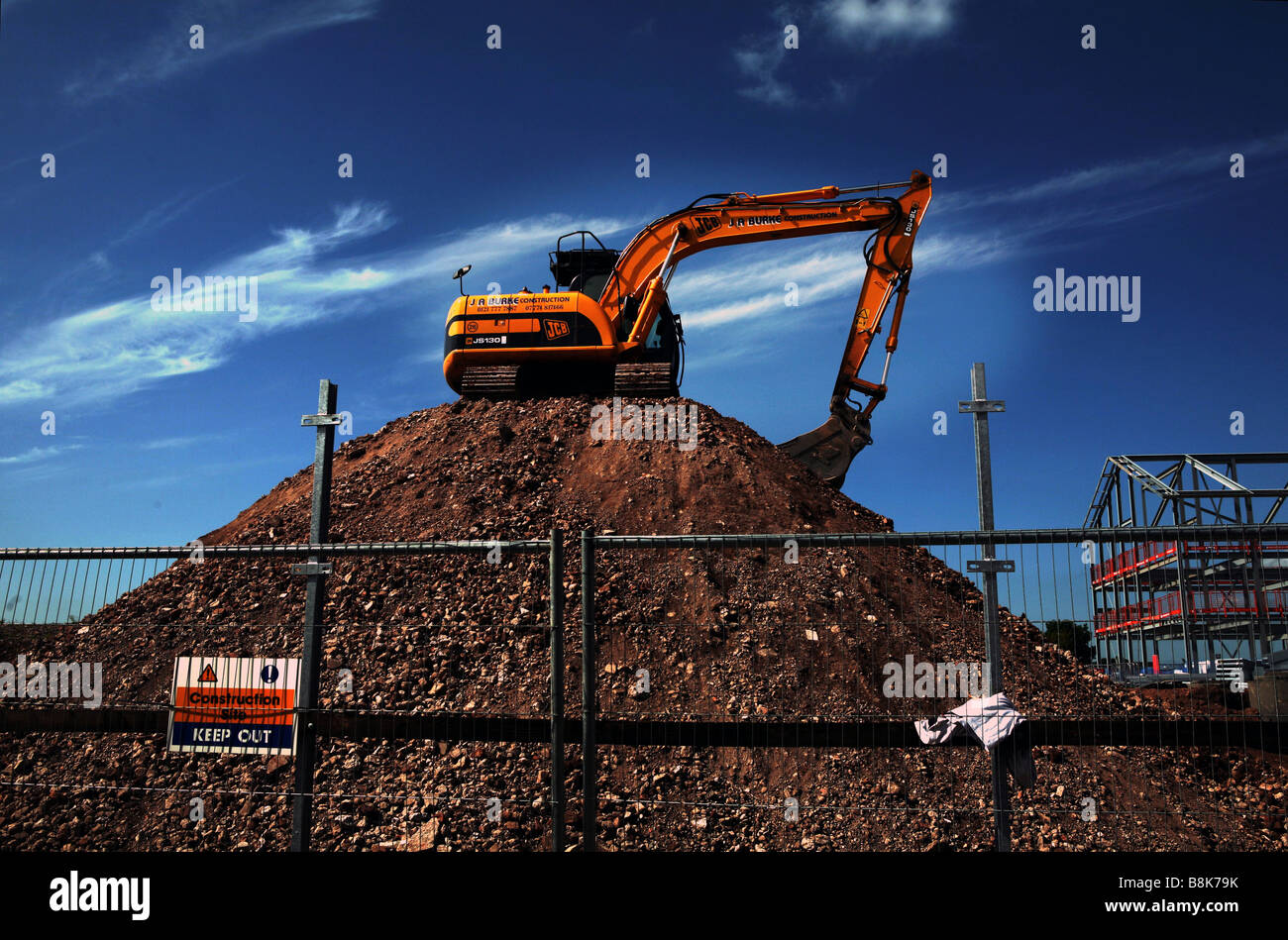 A mechanical digger sits atop a pile of rubble on a building site in England Stock Photo