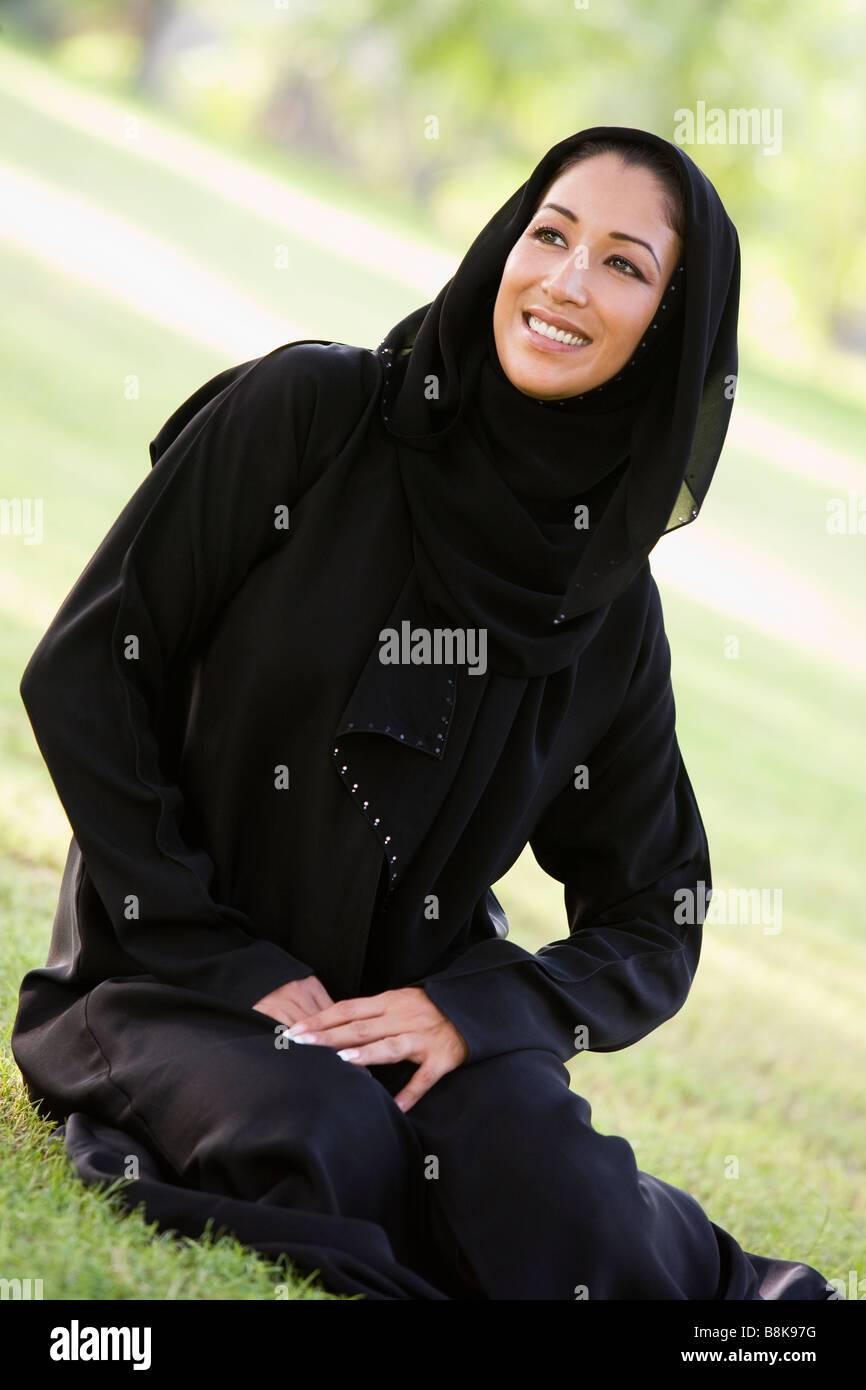 Woman sitting outdoors in park smiling (selective focus) Stock Photo