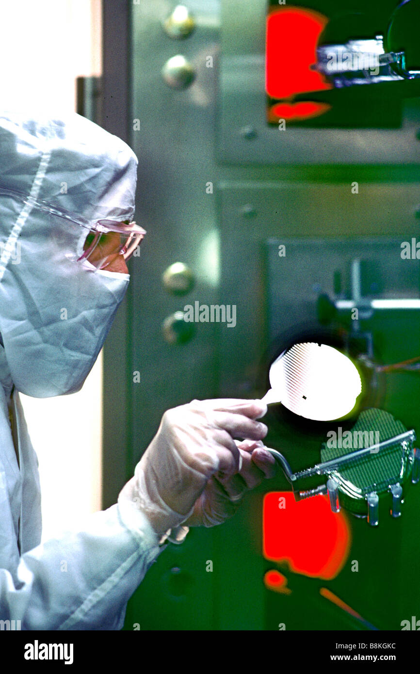 Clean room worker with silicon wafer and ovens in chip production factory. Stock Photo