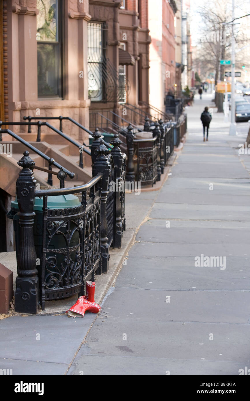 A discarded pair of childrens red boots sit abandoned on a city sidewalk while a person walks away in the distance. Stock Photo