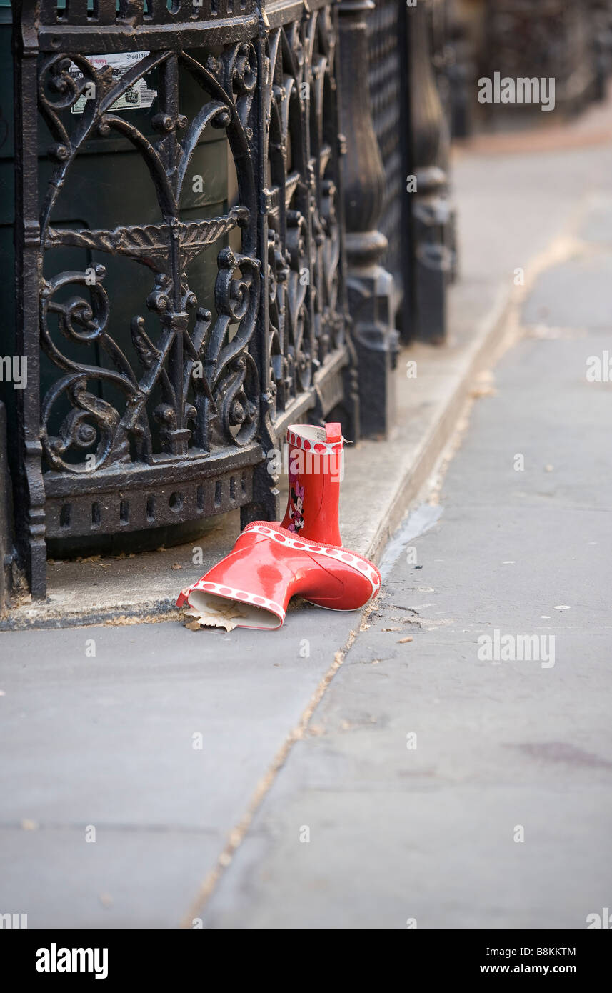 A discarded pair of childrens red boots sit abandoned on a city sidewalk. Stock Photo