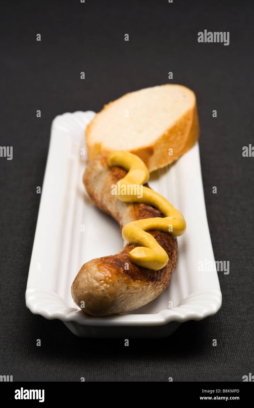 german Thuringer Bratwurst with mustard and slice of bread on serving dish, placed on black textile background, frontal view Stock Photo