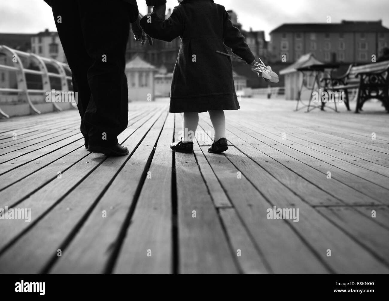 Generations of love: an elderly man walks hand-in-hand with his grand-daughter on an English seaside pier Stock Photo