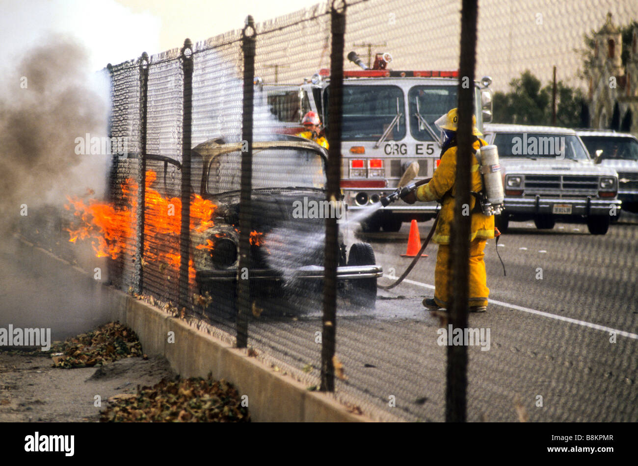 Volkswagen bug auto goes up in flames as fire fighter works to extinguish flames emergency respond response Stock Photo