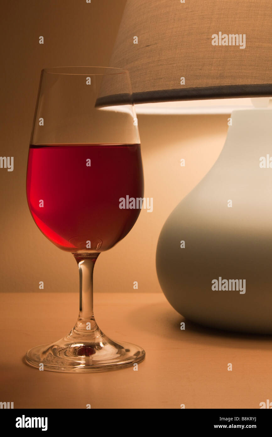 Glass of red wine with lit table lamp in the evening switched on. Homely concept. England UK Stock Photo