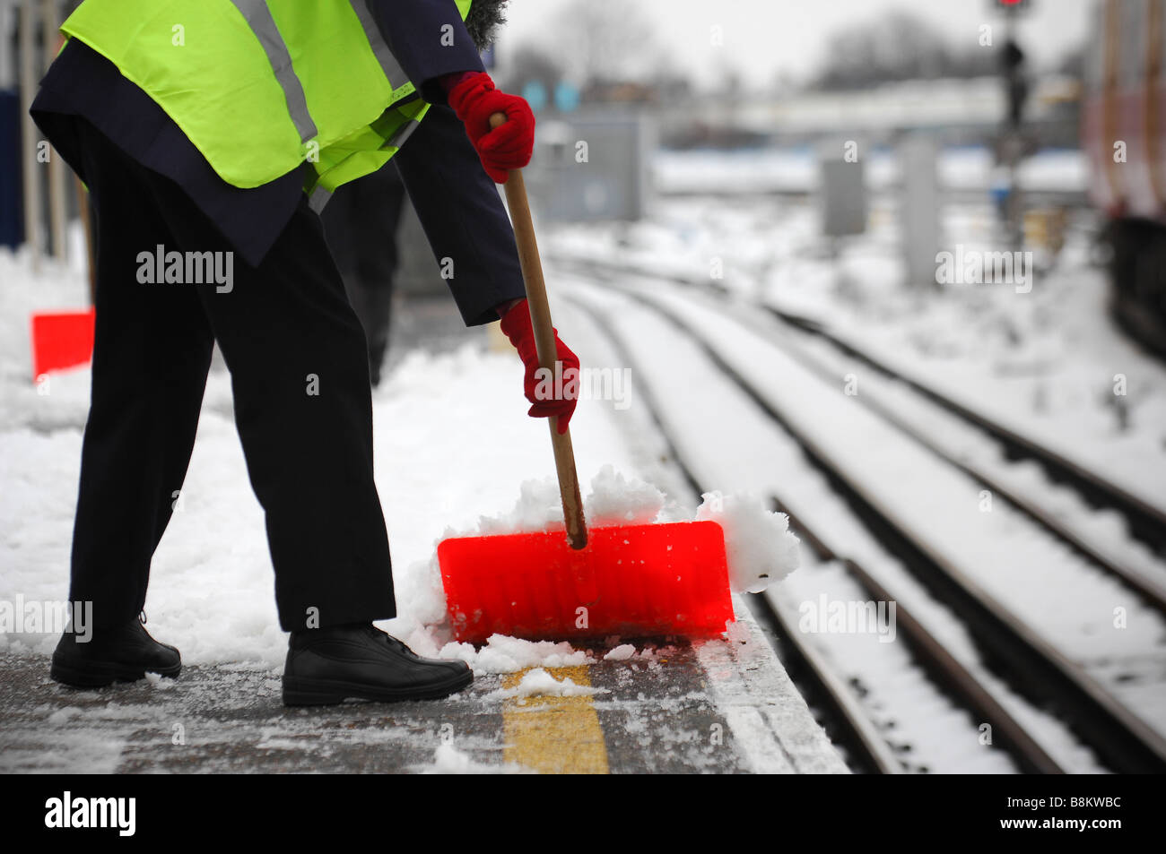 A railway maintenance worker clears the snow covered platform at Wimbledon station, south west London. Stock Photo