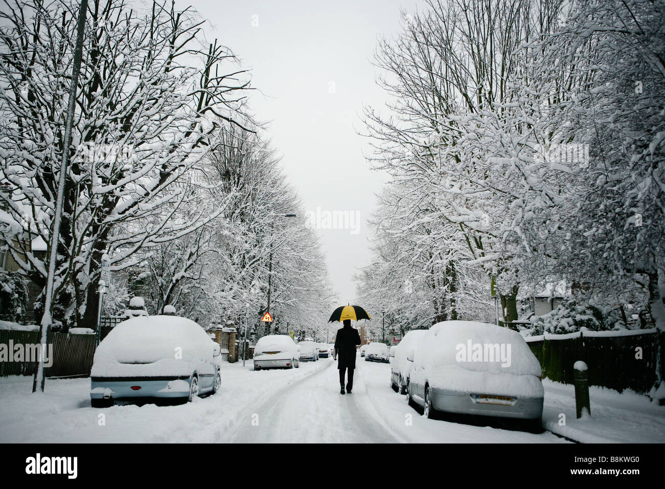 A commuter with umbrella makes his way to work on a snowy winter's morning in East Putney, London, UK. Stock Photo