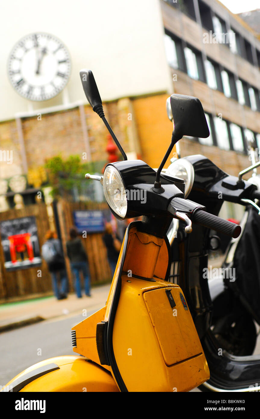 A line of Vespa scooters in Shorditch, East London, on a roadside with a city background. Stock Photo