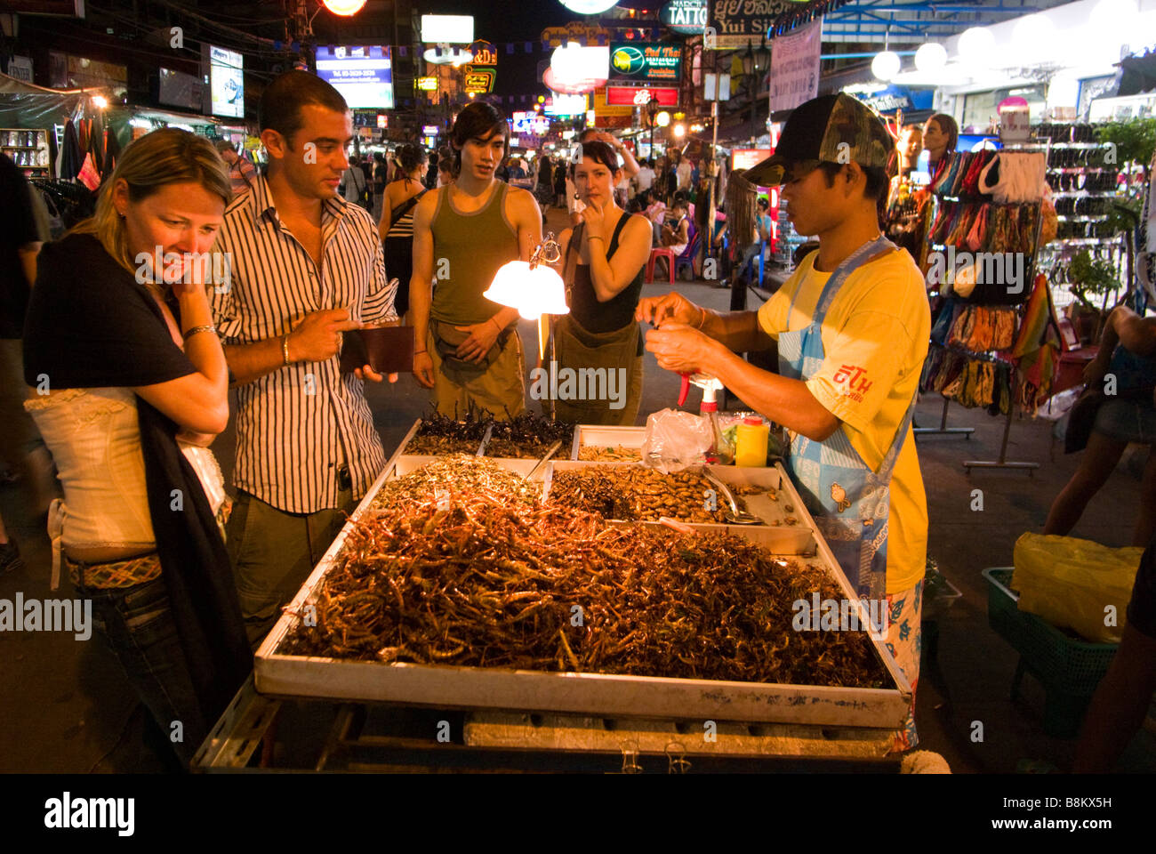 Tourists buying fried insects at night market food stall Khao San Road in Bangkok Thailand Stock Photo