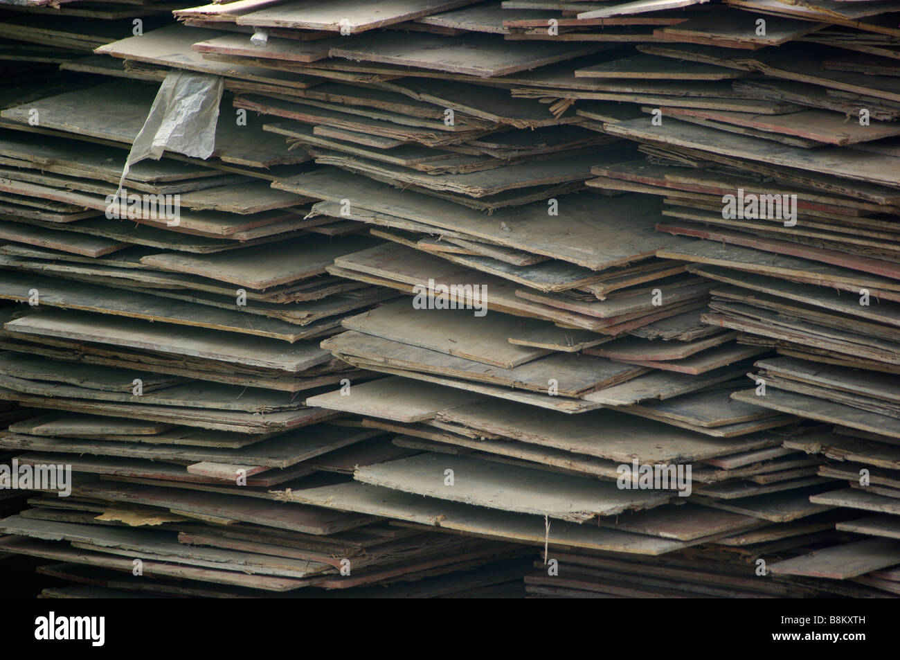 A stack of boards, wood, planks and plywood is stacked in an industrial construction site where a massive building project sits. Stock Photo