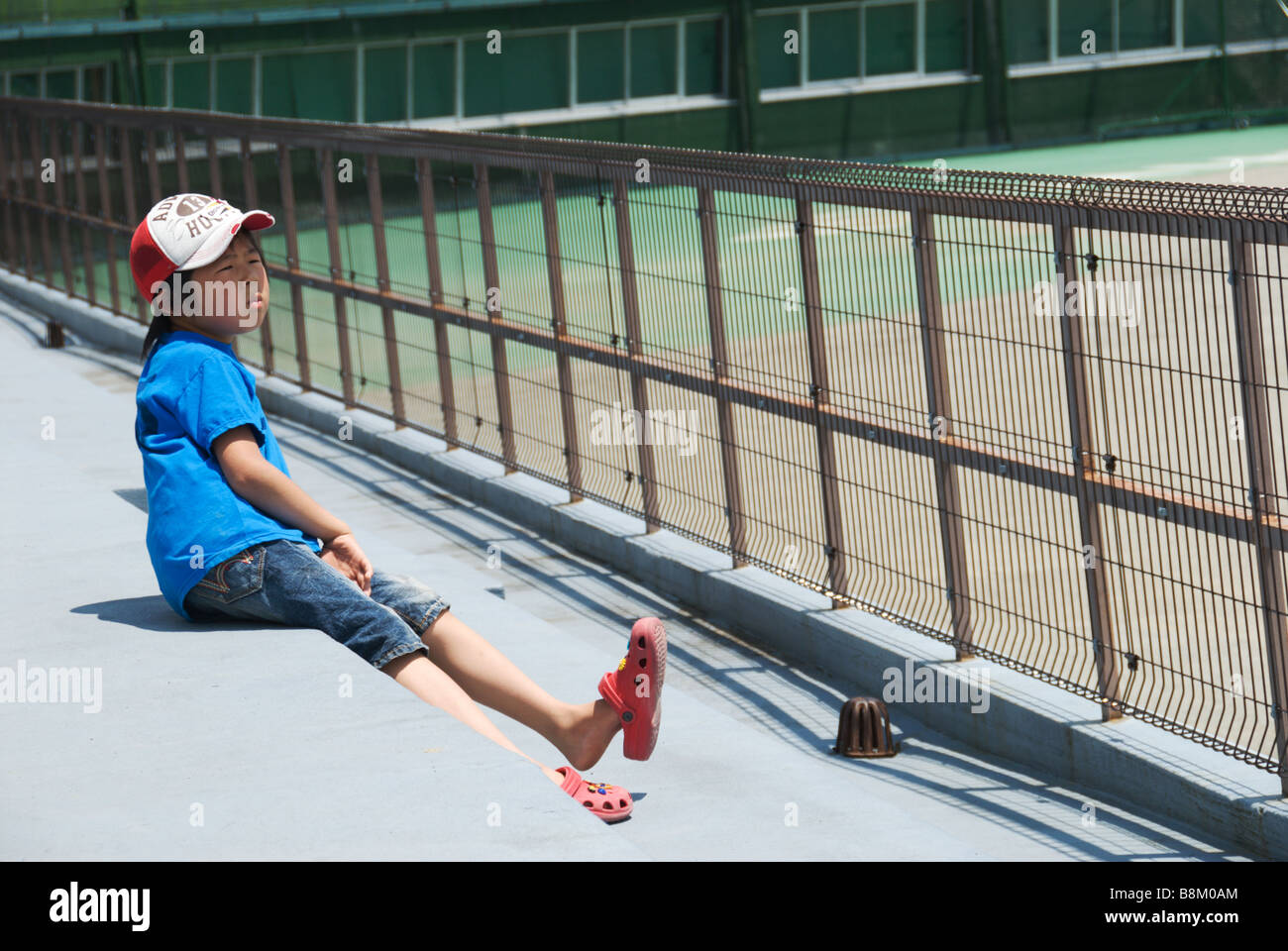 A Japanese girl swings her legs in the grandstands at a small town baseball stadium, Shimosuwa Stock Photo