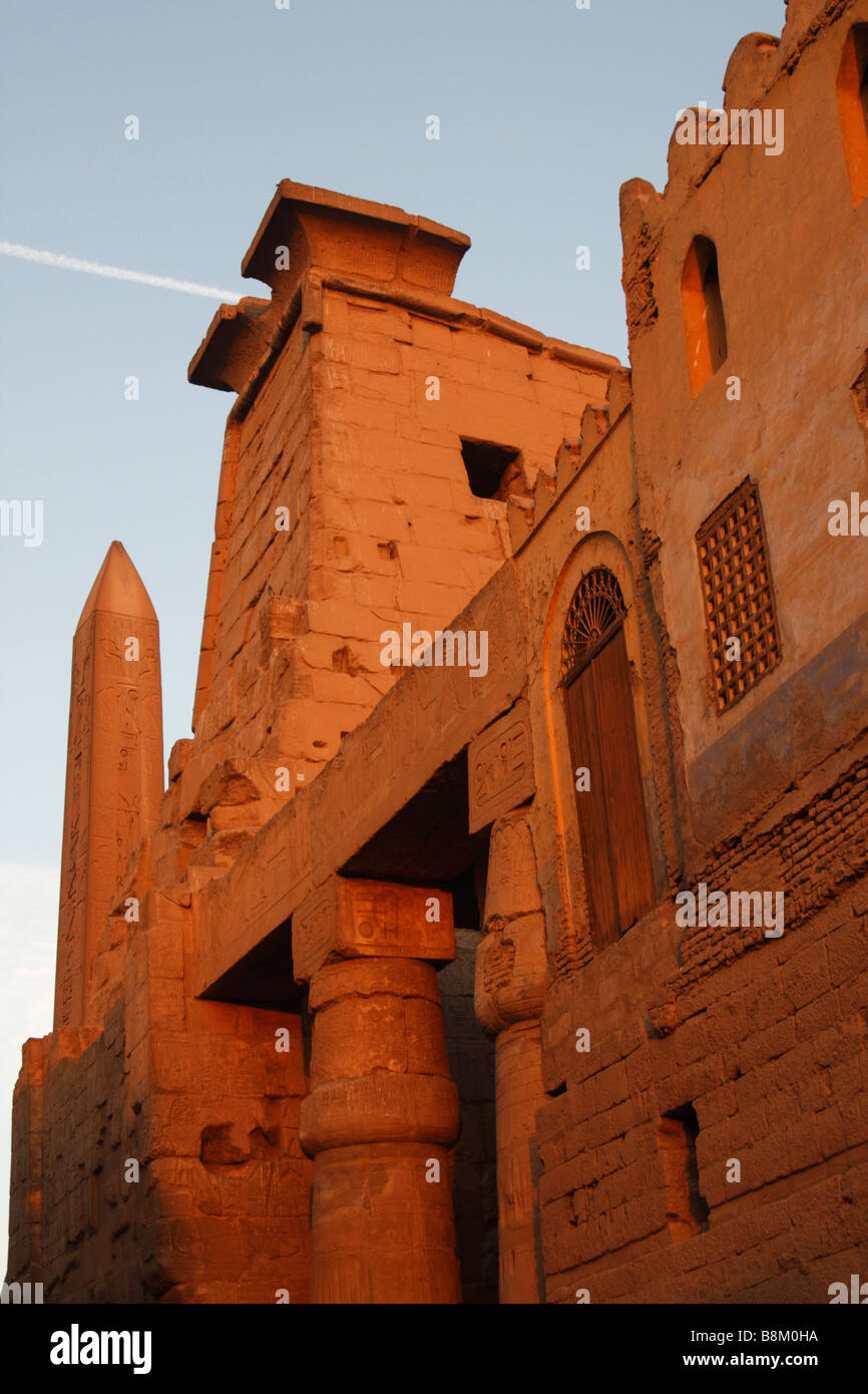 Egypt, Luxor temple ruins, [low angle] view of obelisk, first pylon and mosque wall lit by orange glow of sunset Stock Photo