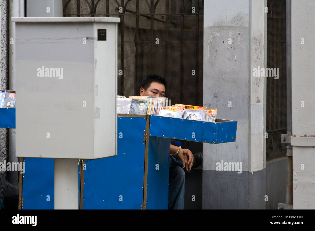 Street vendor hiding behind his stall of pirate DVDs in Shanghais french concession. Stock Photo