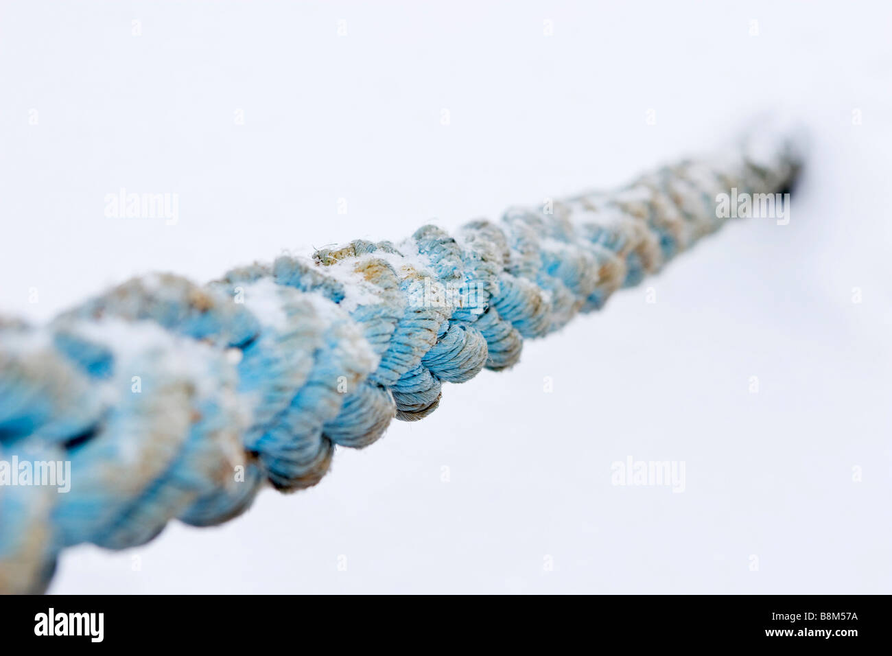 Old stron blue towing cable anchored to the frozen covered with ice river in winter time. Stock Photo