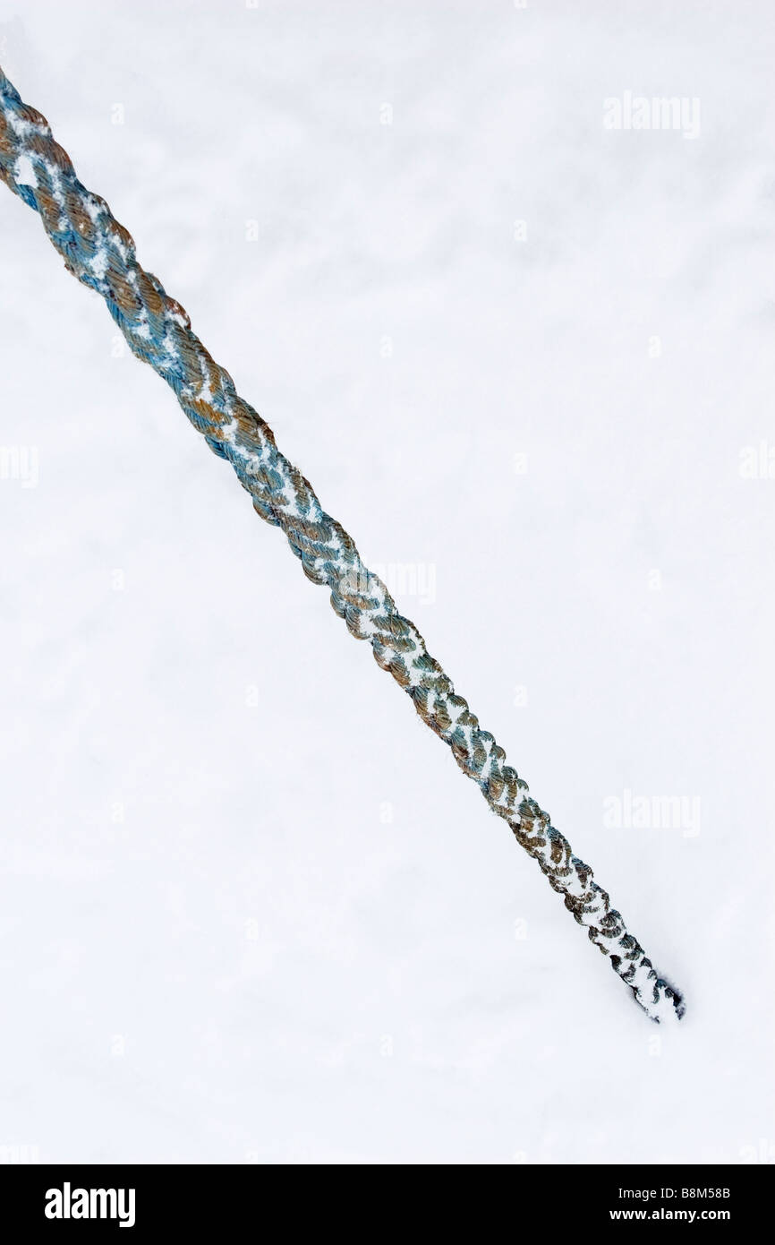 Old stron blue towing cable anchored to the frozen covered with ice river in winter time. Stock Photo
