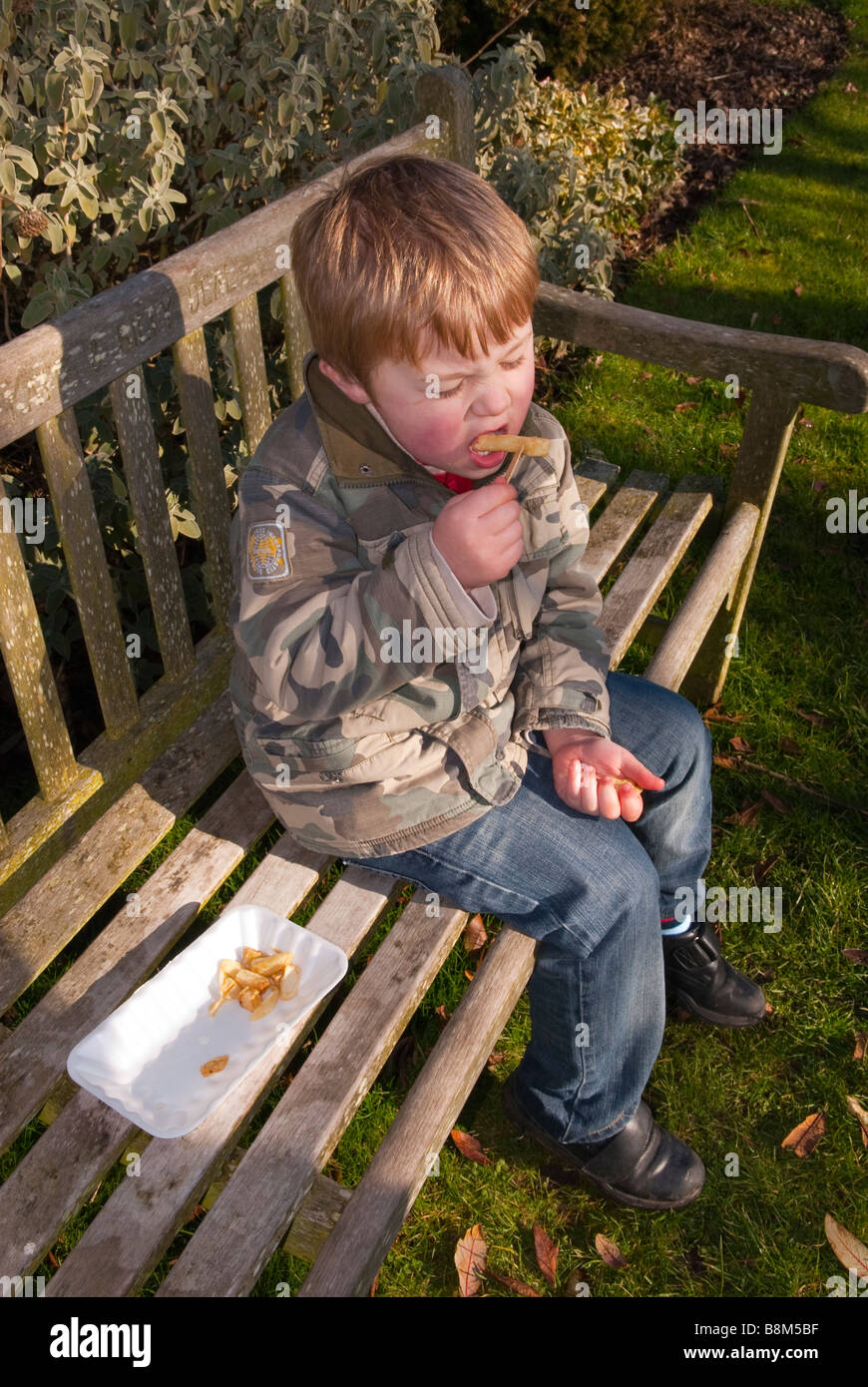 Young boy child eating his chips outdoors on a park bench Stock Photo