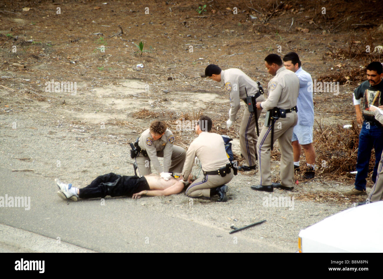 California Highway Patrol officers adminsister CPR to handcuffed prisoner on side of highway. Stock Photo