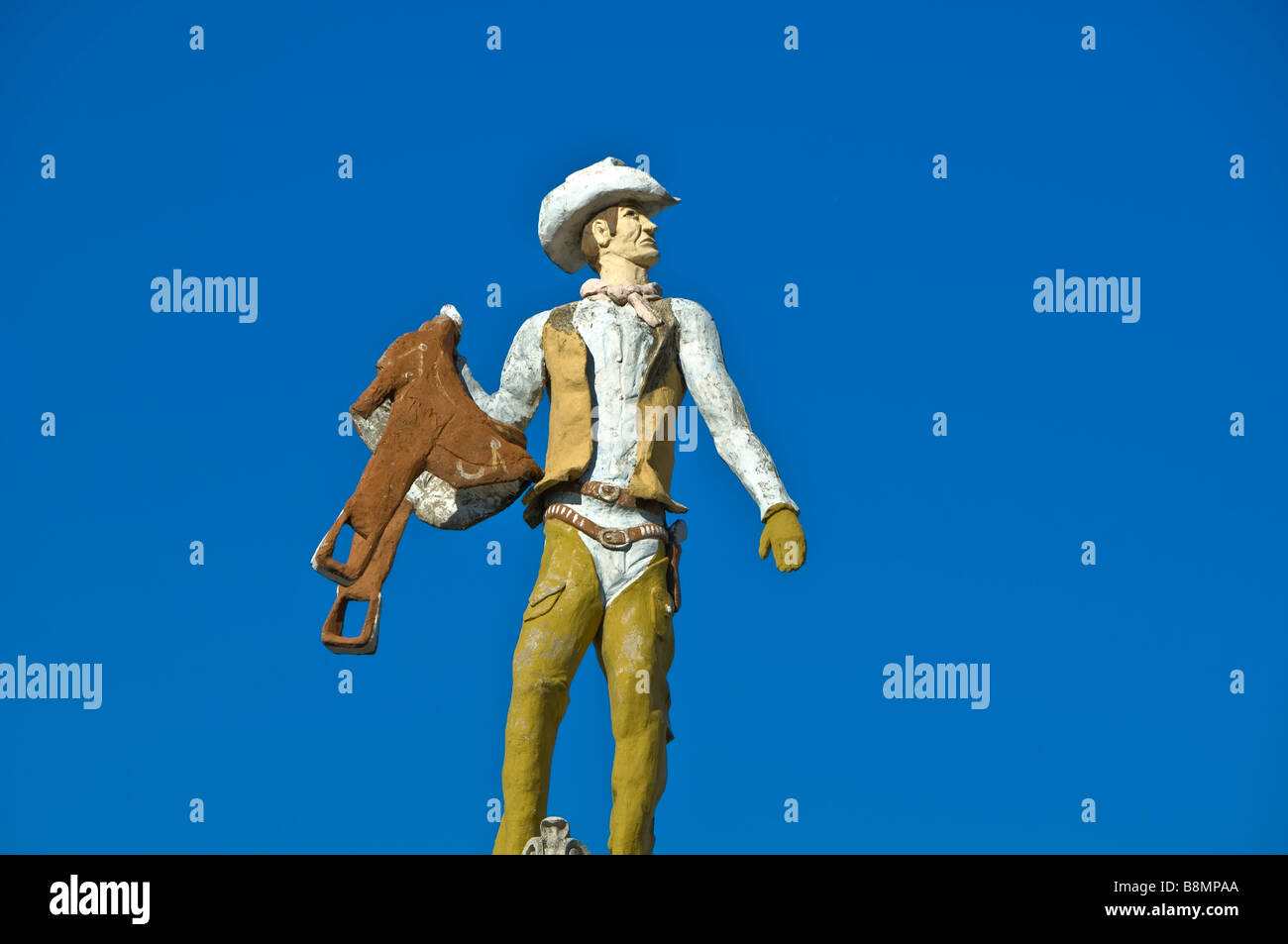 Statue of American Cowboy with cowboy hat leather vest holding saddle with clear blue sky background San Antonio Texas tx Stock Photo