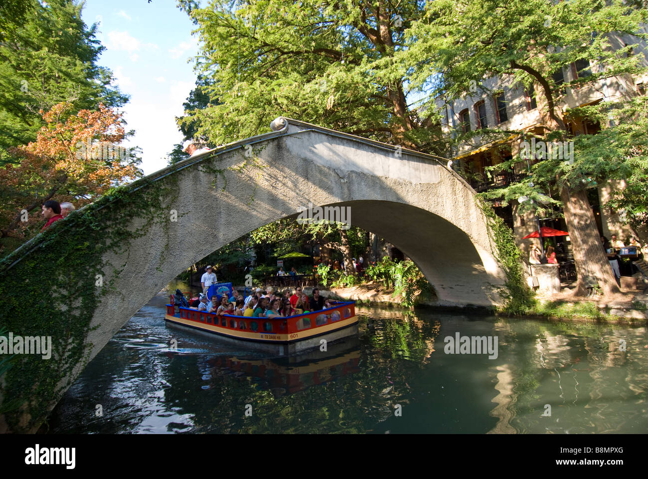 San Antonio Riverwalk boat goes under bridge on San Antonio River bright sunny day Stock Photo
