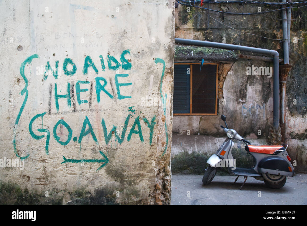 AIDS slogan graffiti on the wall and a scooter in the historic centre of UNESCO listed Stone Town in Zanzibar, Tanzania Stock Photo