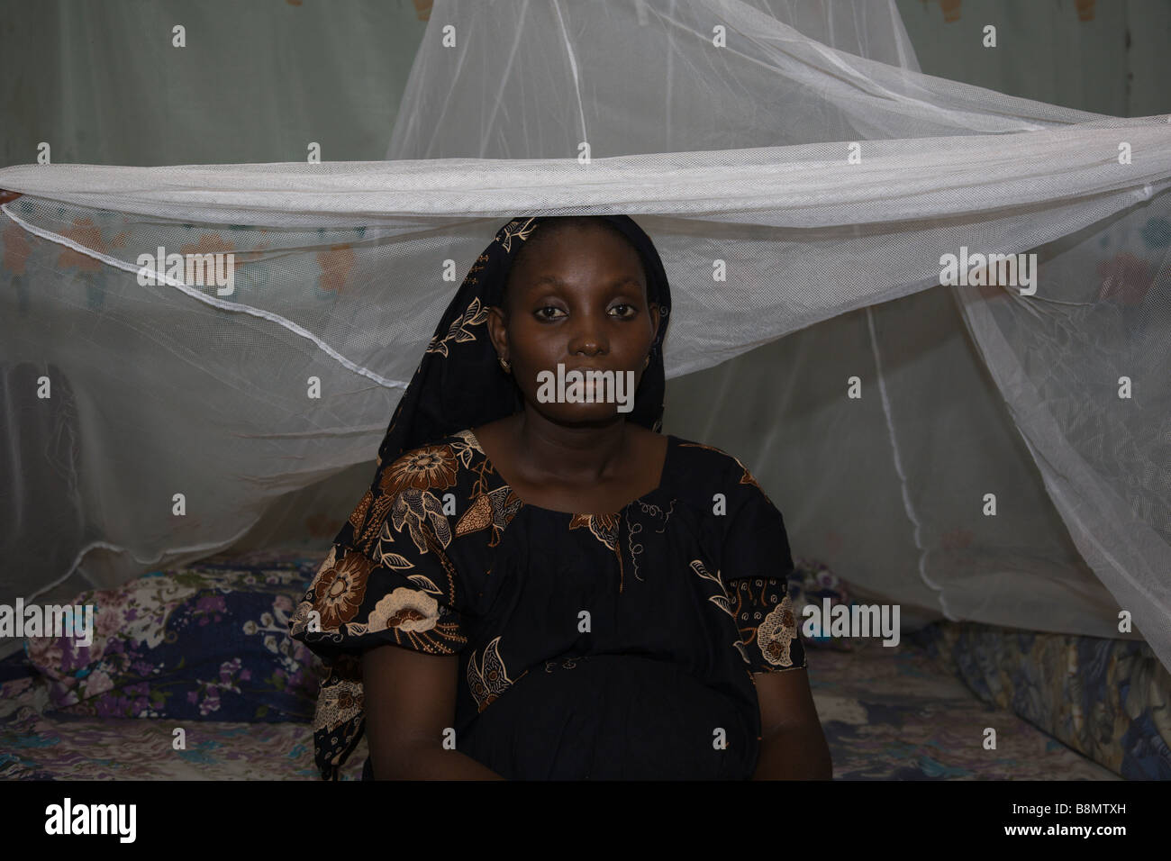 A pregnant woman sleeps under a mosquito net every night, preventing malaria, which is transmitted through mosquito bites. Stock Photo