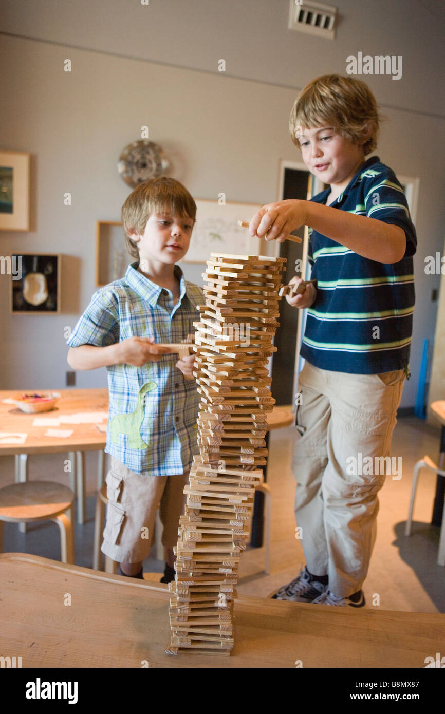 two boys working together,  attempting to build a tall tower out of wooden blocks Stock Photo
