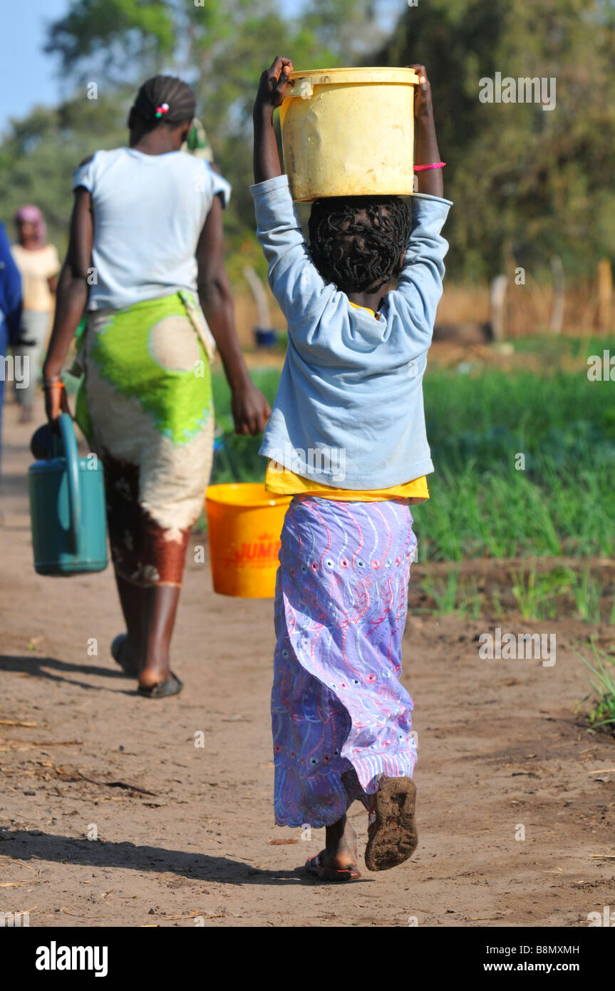 Child carries a bucket of water on her head, The Gambia, West Africa