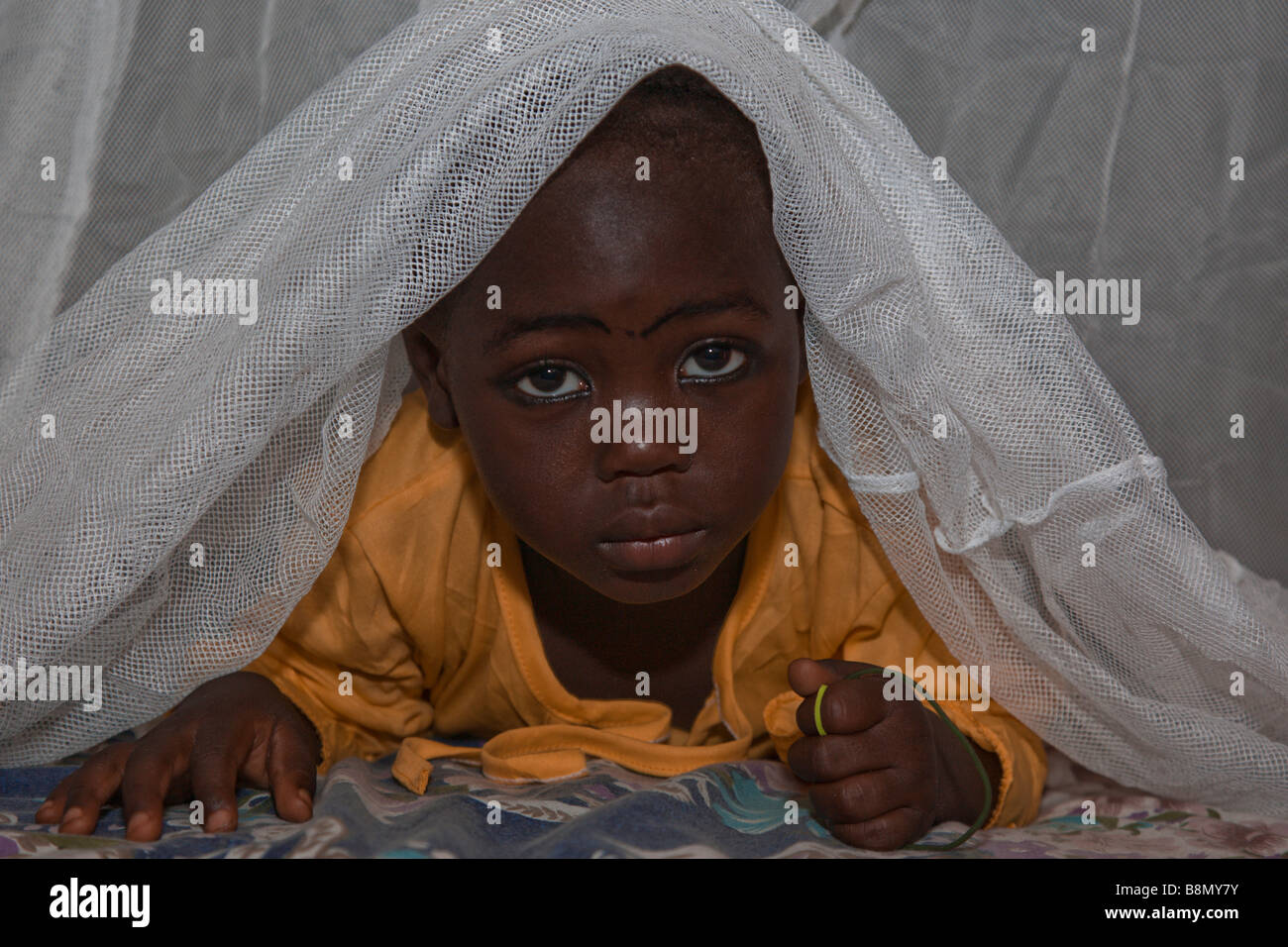 A child in the Garki area of Abuja peeks out from under a Permanet long lasting insecticide treated mosquito net. Stock Photo