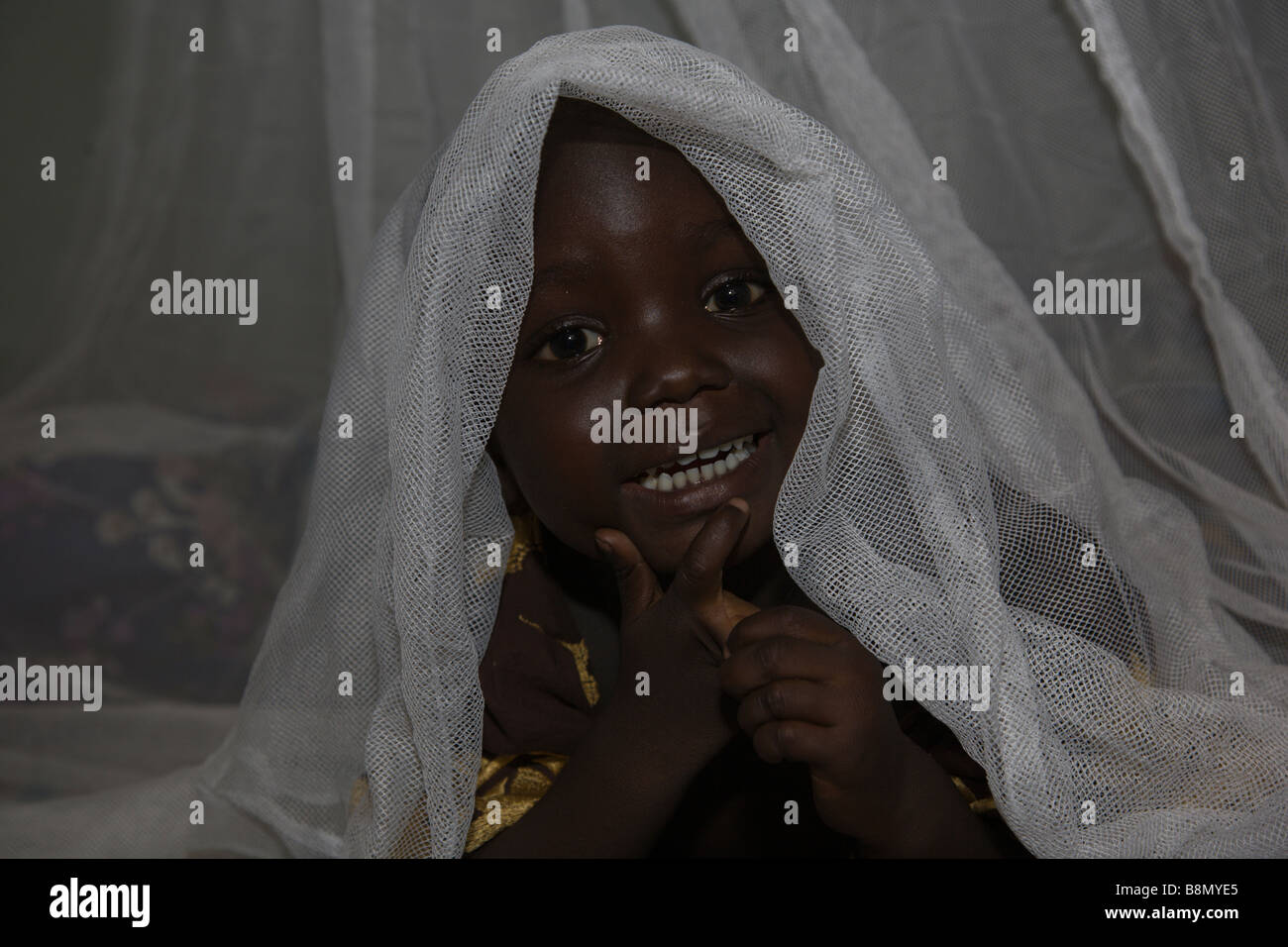 A child in the Garki area of Abuja peeks out from under a Permanet long lasting insecticide treated mosquito net. Stock Photo