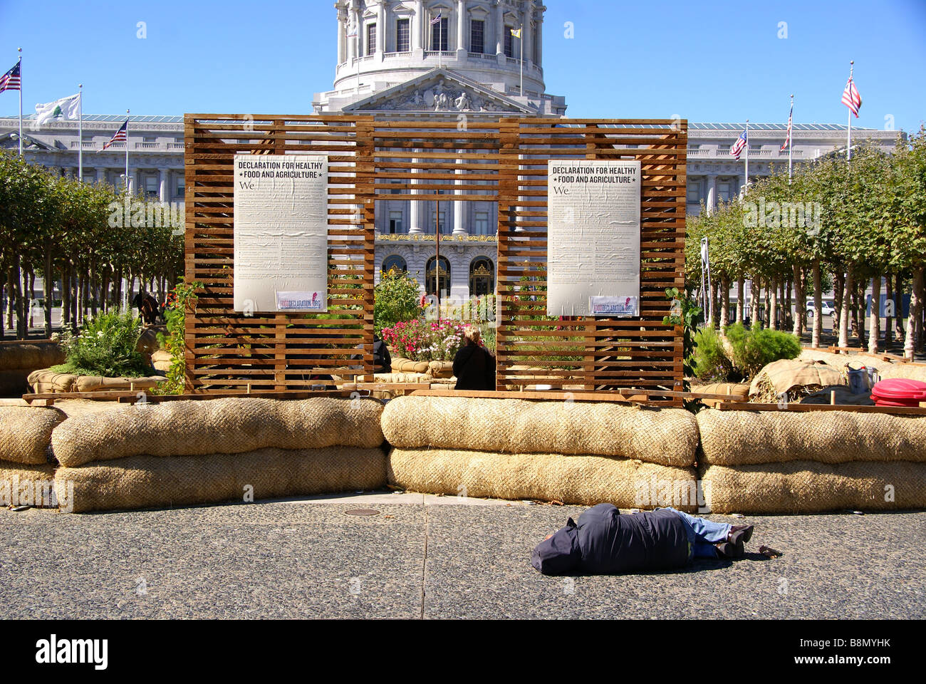 Homeless person sleeps in front of "Declaration for healthy food and agriculture" sign by city hall in San Francisco Stock Photo