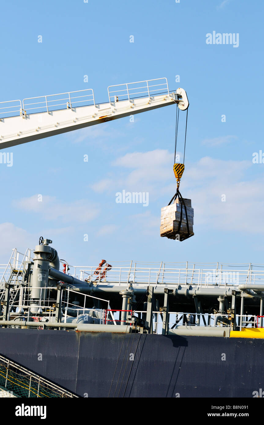 Crane lifting a pallet of supplies, provisions and cargo onto a 'oil tanker' ship Stock Photo