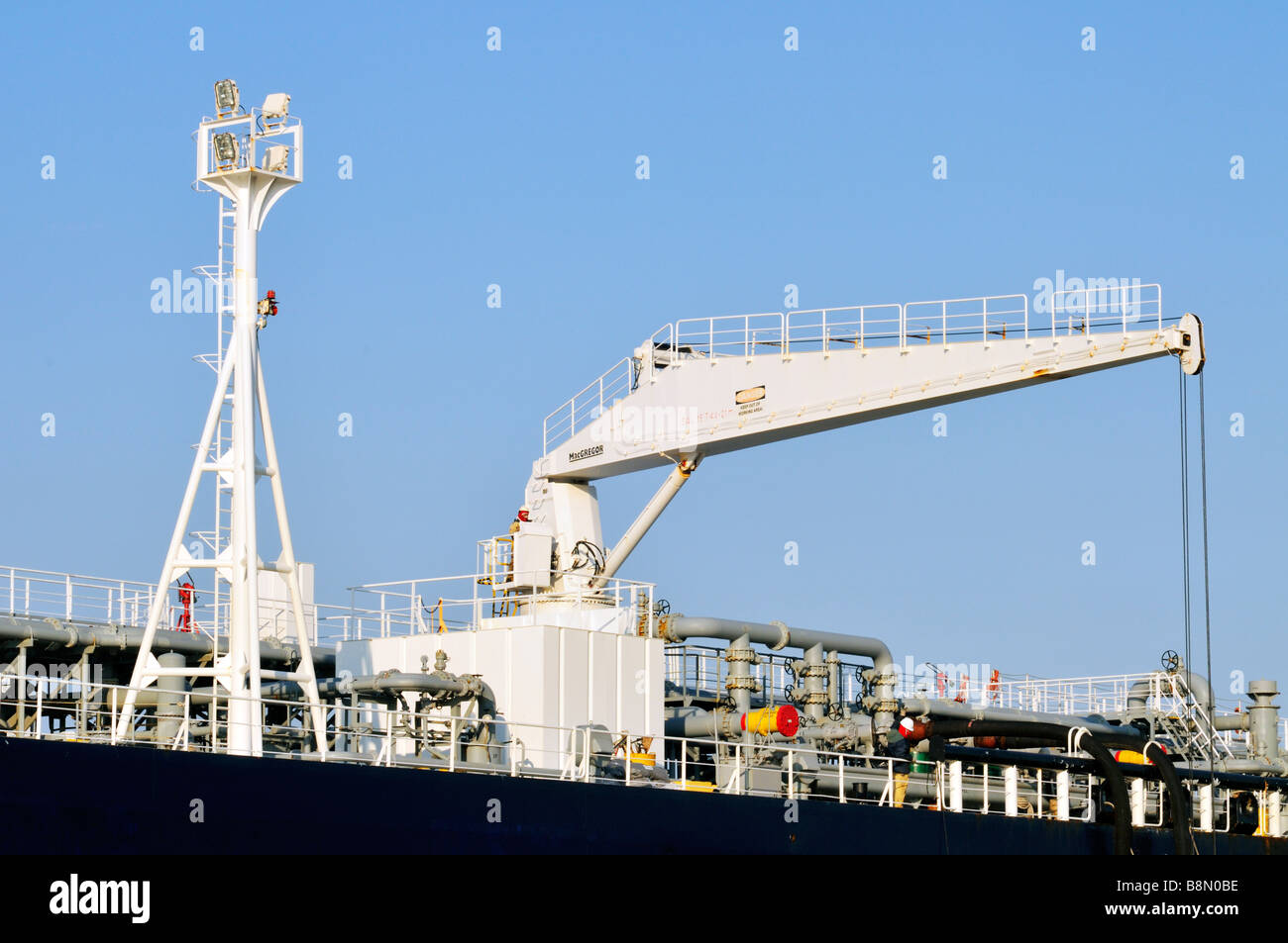 Deck of 'oil tanker' with crewmen operating a [hydraulic hose handling crane] showing tower mounted work lights and oil pipeline Stock Photo