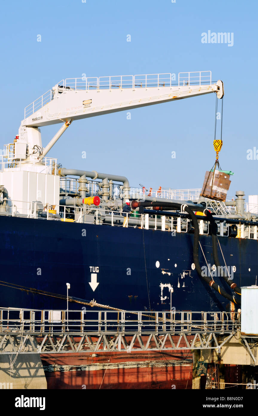 Crane loading pallet of supplies or provisions on ship and oil being