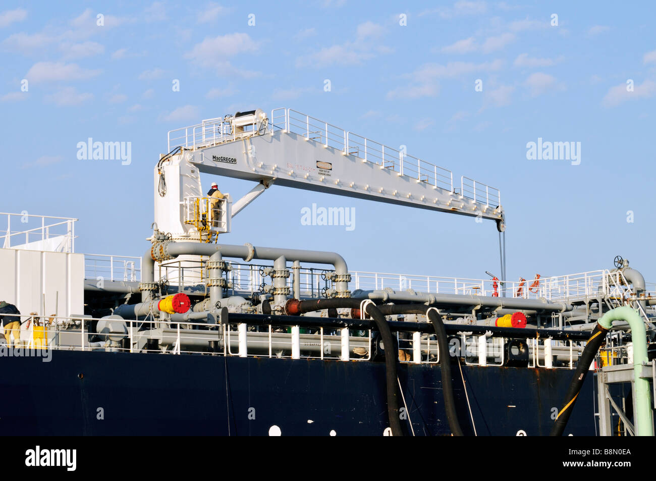 Workers operating a [hydraulic hose handling crane] on the deck of an