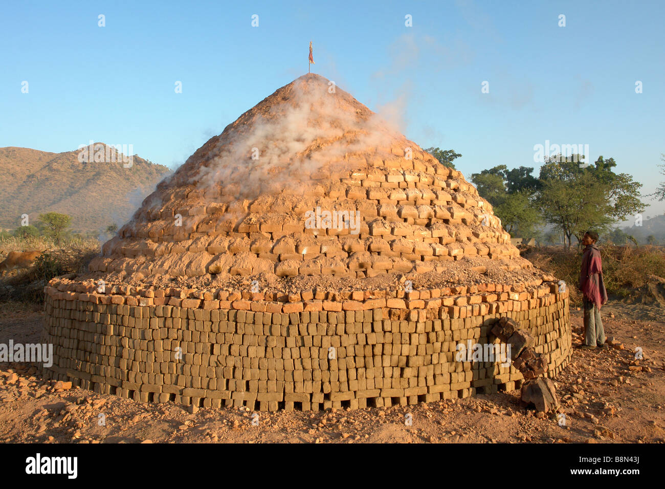 worker at a traditional indian clay brick kiln smoking by dawn light Stock Photo