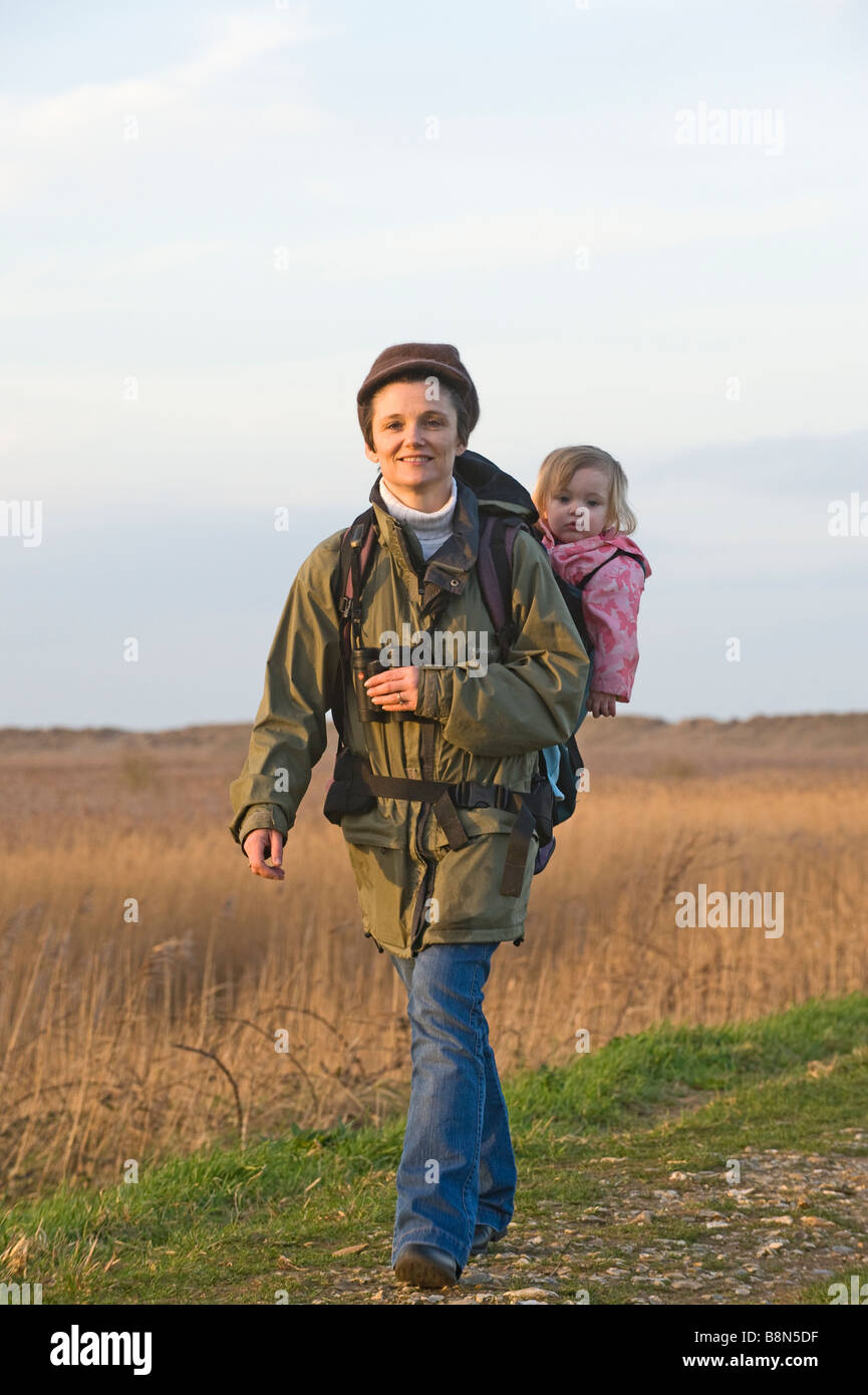 mother carrying toddler in backpack while bird watching along coastal path North Norfolk winter Stock Photo