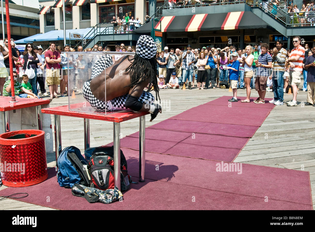 Street performer climbing into a transparent glass box during a contortionist act Stock Photo
