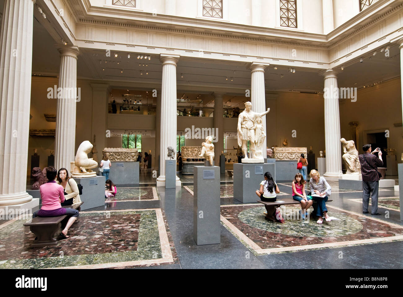 Visitors to the Metropolitan Museum of Art sitting on benches in an internal courtyard surrounded by classical sculptures Stock Photo