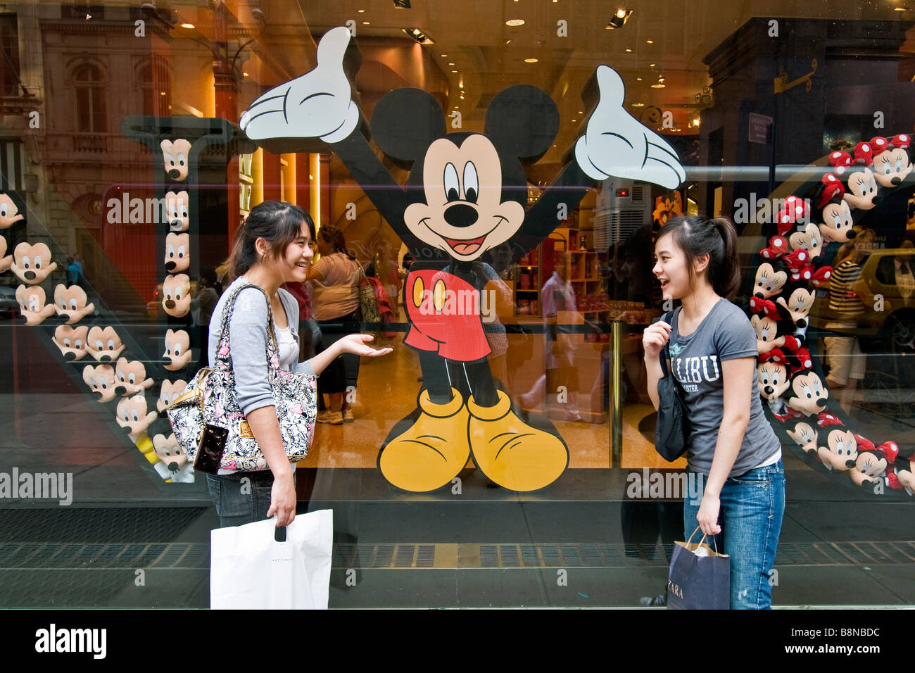 Two young Japanese girls chatting outside a Mickey Mouse window display on 5th Avenue Stock Photo