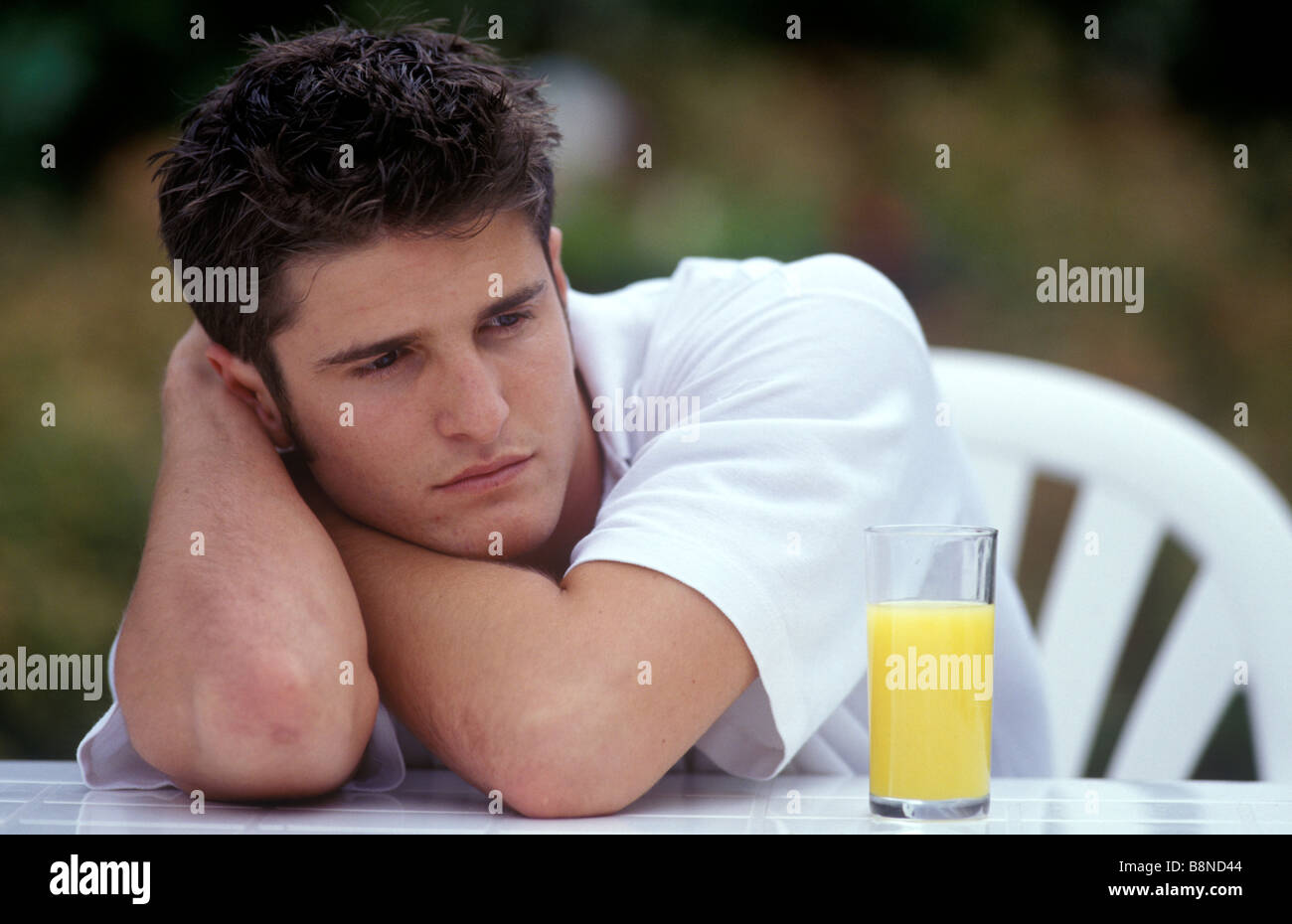 depressed man sitting outside with a glass of orange juice Stock Photo