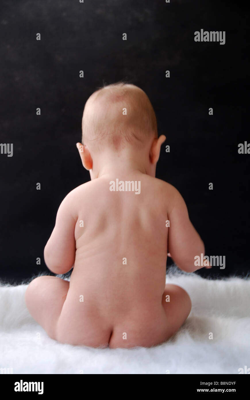 Back of baby sitting naked on a rug Stock Photo