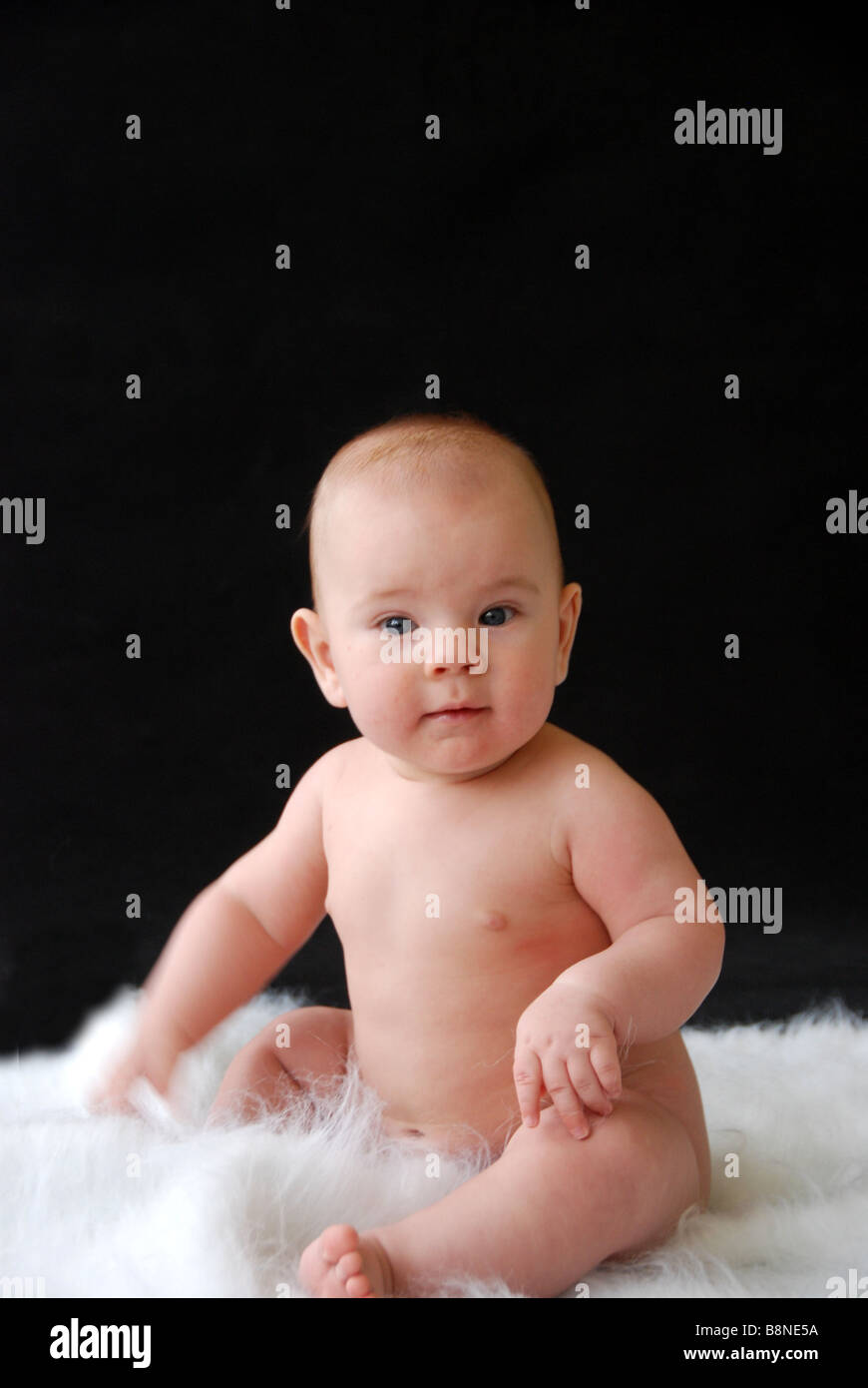 Happy baby sitting naked on a rug Stock Photo
