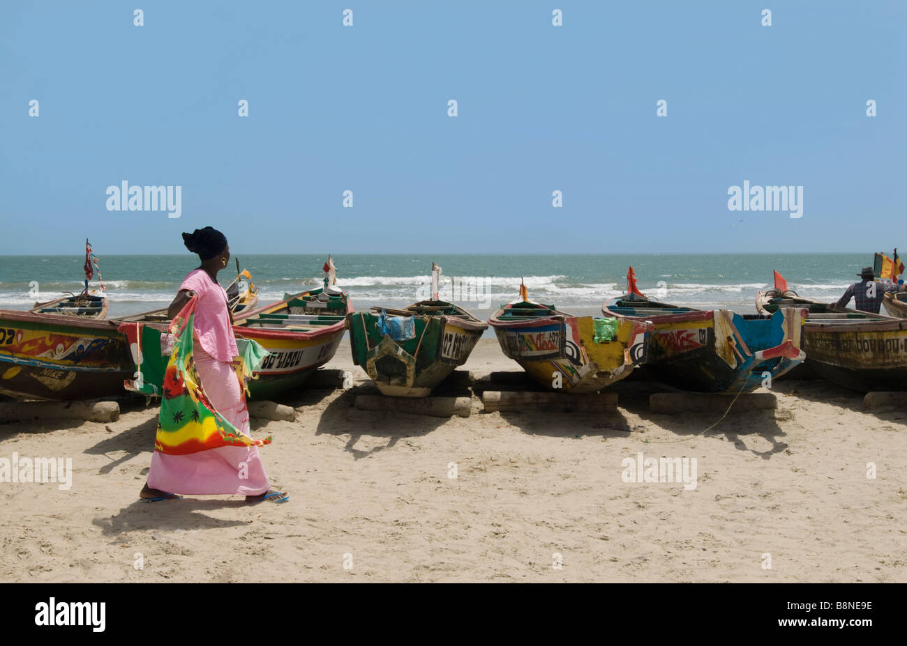 fish boats on the beach with woman in pink traditional dress walking casamance cap skirring Stock Photo