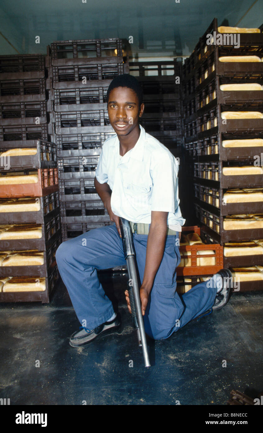 An armed guard holds his shotgun ready as he kneels in the back of a bread delivery van Stock Photo