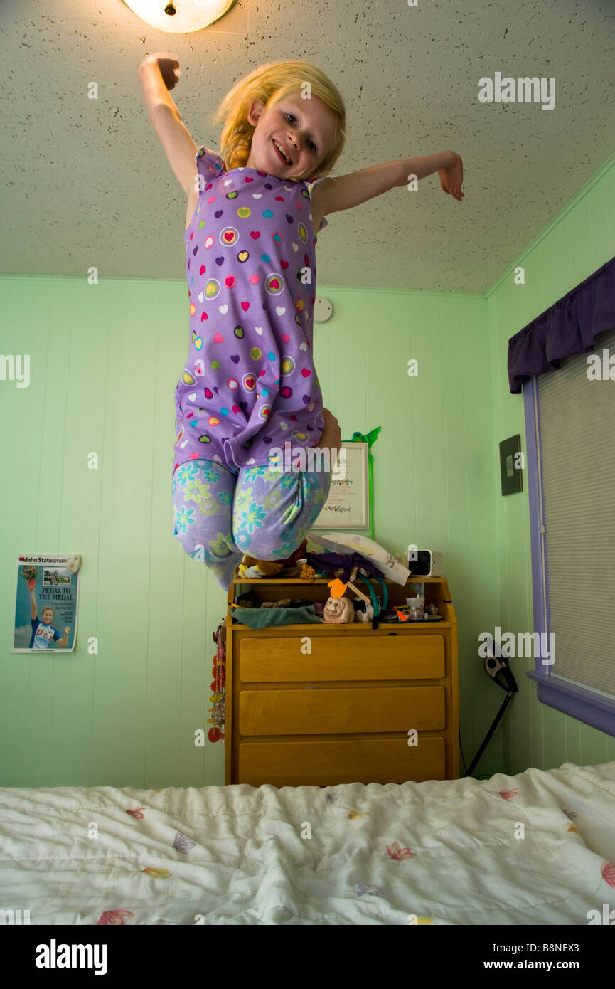 Young girl jumping on a bed in a bedroom with green walls Stock Photo