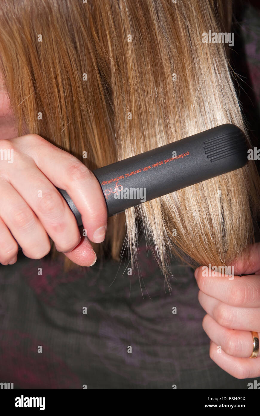 A close up of a woman straightening her hair using Ghd professional straightening irons Stock Photo