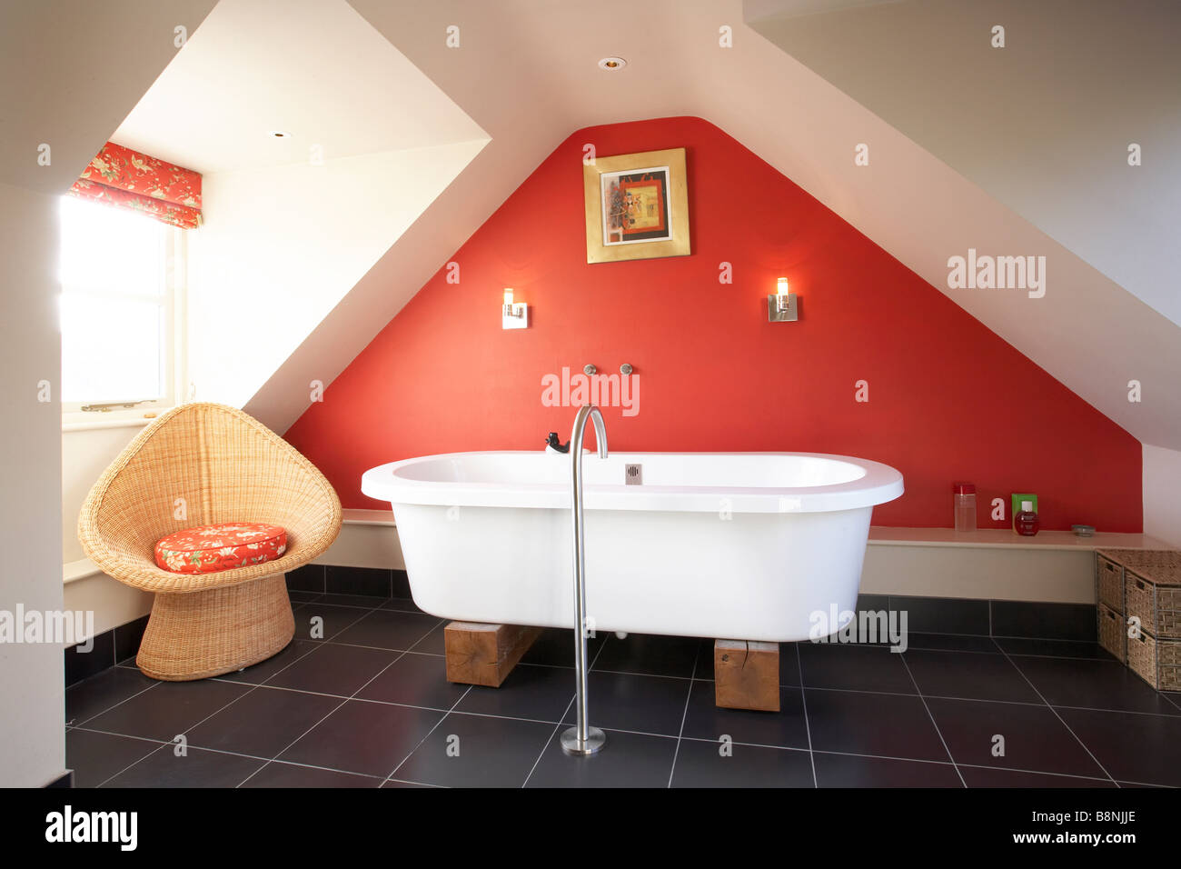 Interior bathroom in attic roof space with modern freestanding bath on wood blocks red wall black slate floor Stock Photo